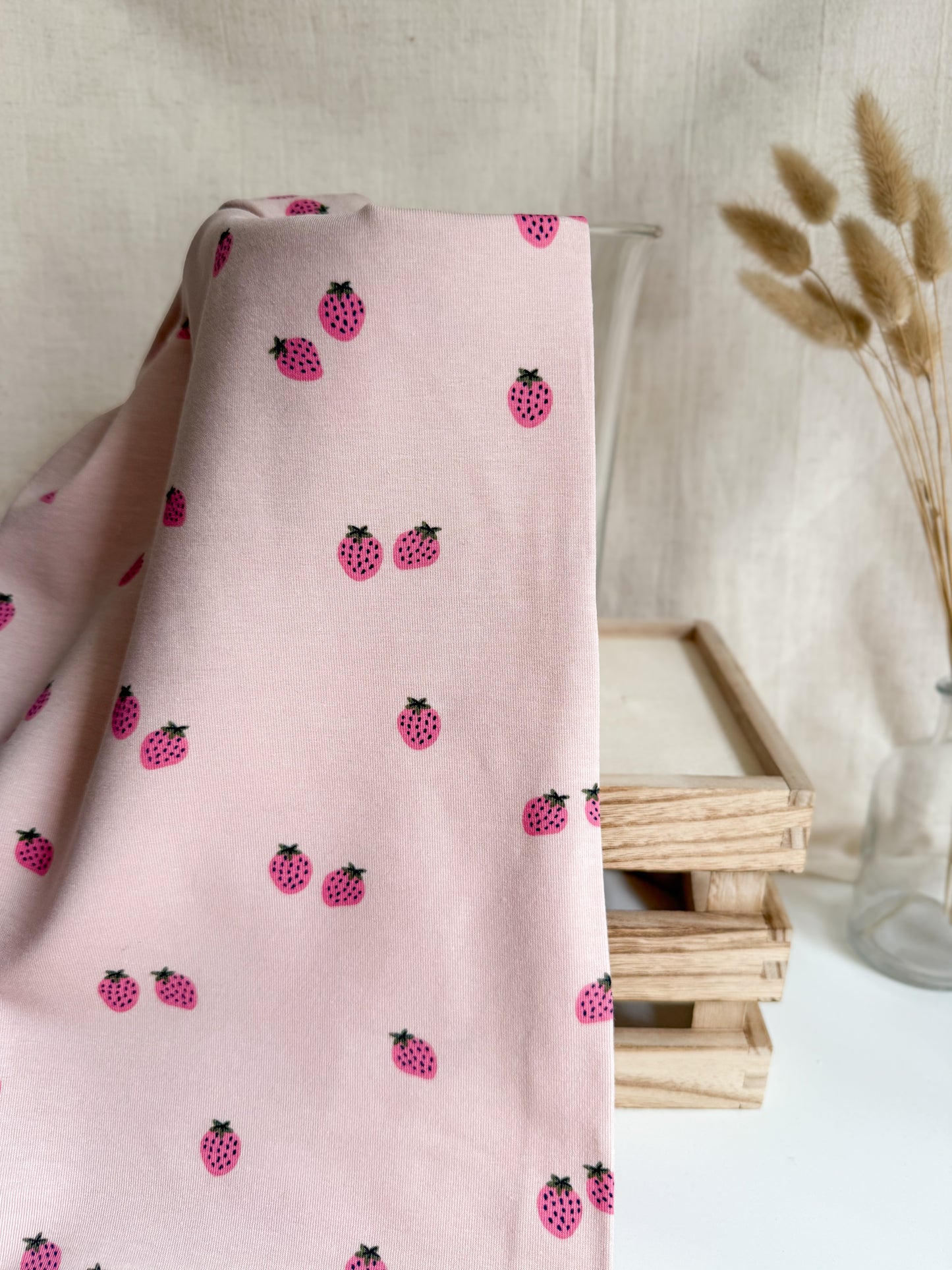 Pink fabric with black and red berry pattern draped over a surface with a neutral background.
