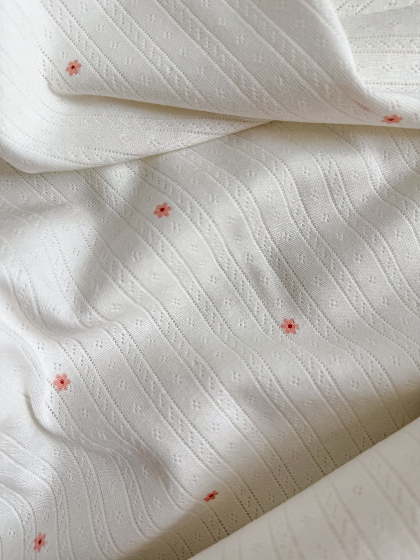 Tiny pink flowers on a white pointelle jersey fabric for sewing T-Shirts and Baby Clothing and Pyjamas