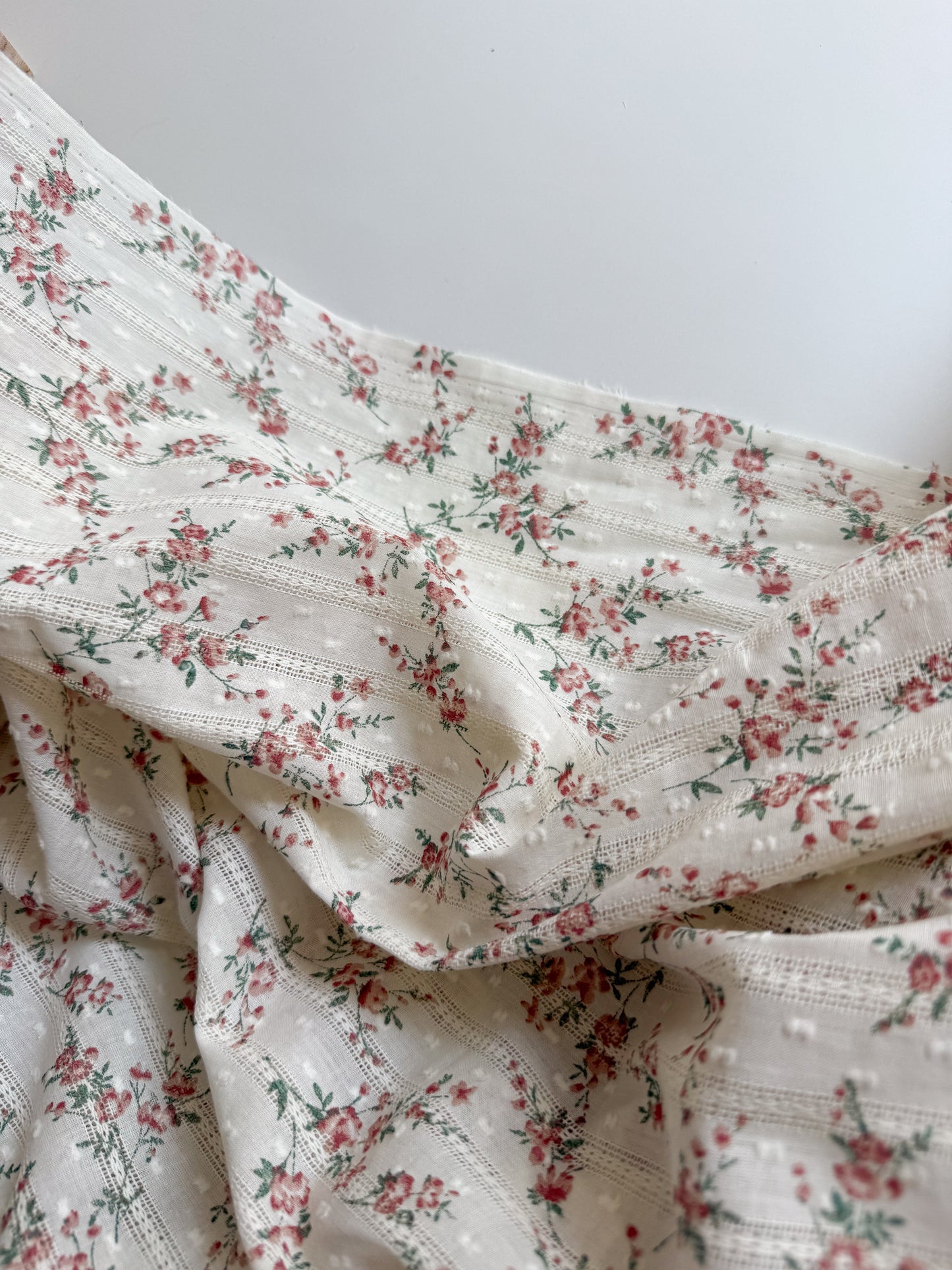 Close up of red floral print on soft cotton embroidered dobby swiss dot fabric