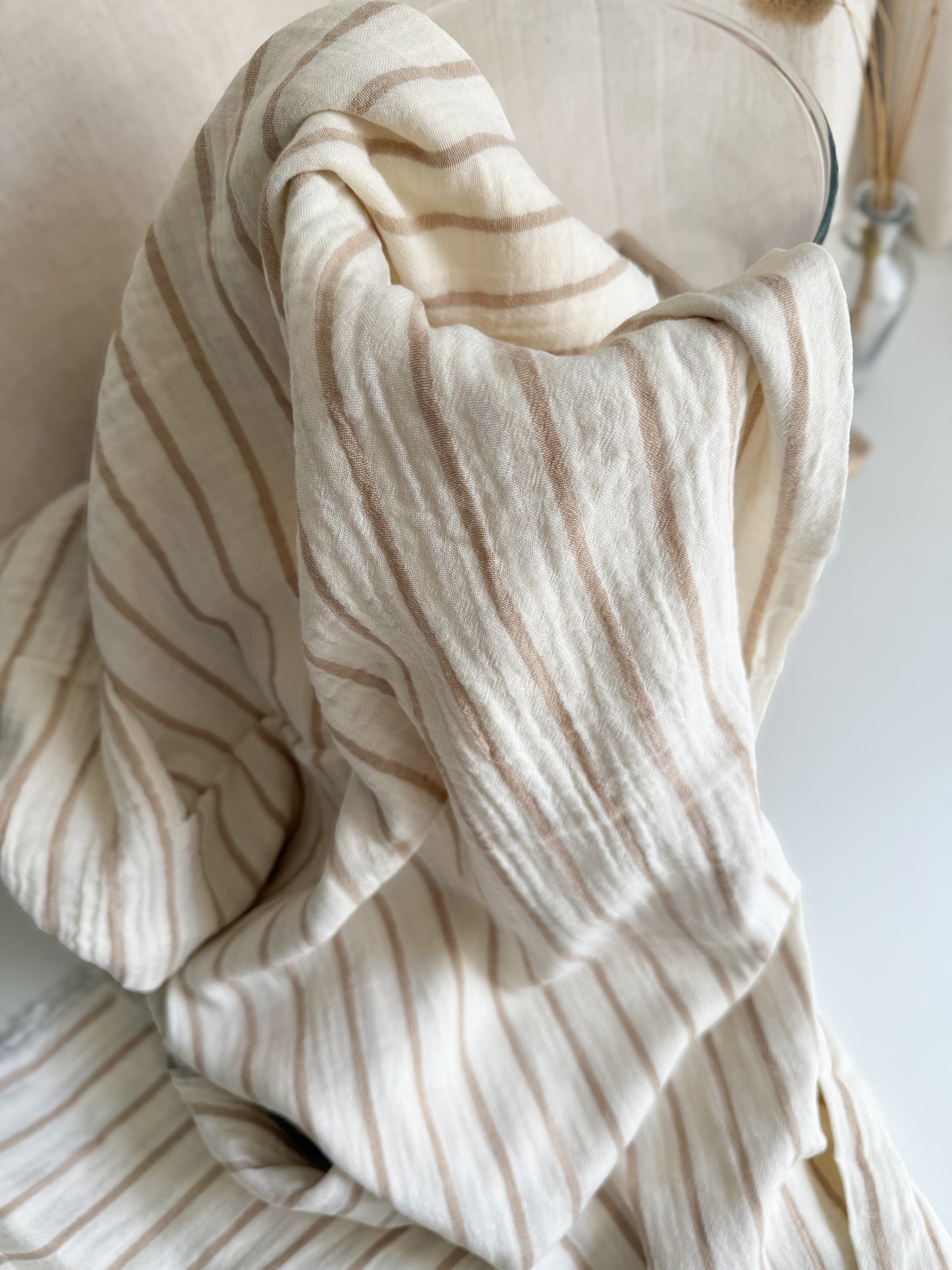 Beige stripe double gauze muslin sewing fabric on an off white background
