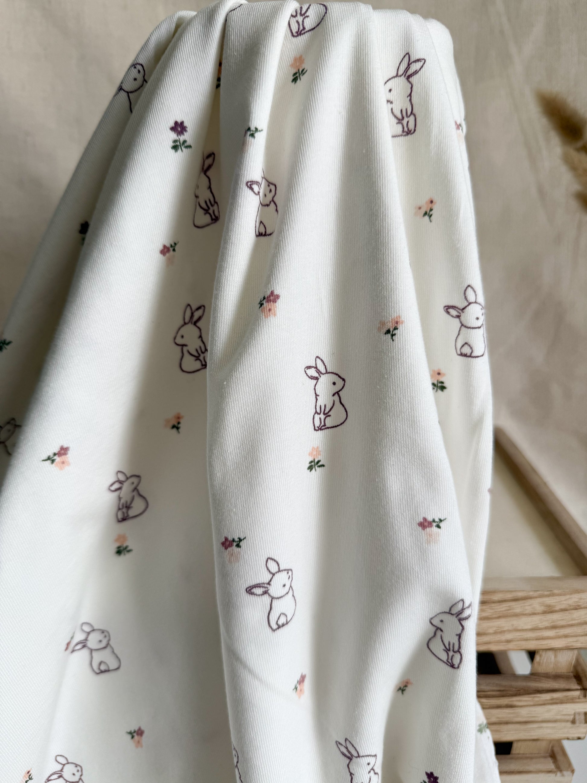 A cotton jersey fabric on an off-white background with s cute bunny rabbit and floral print in purple and pink. 