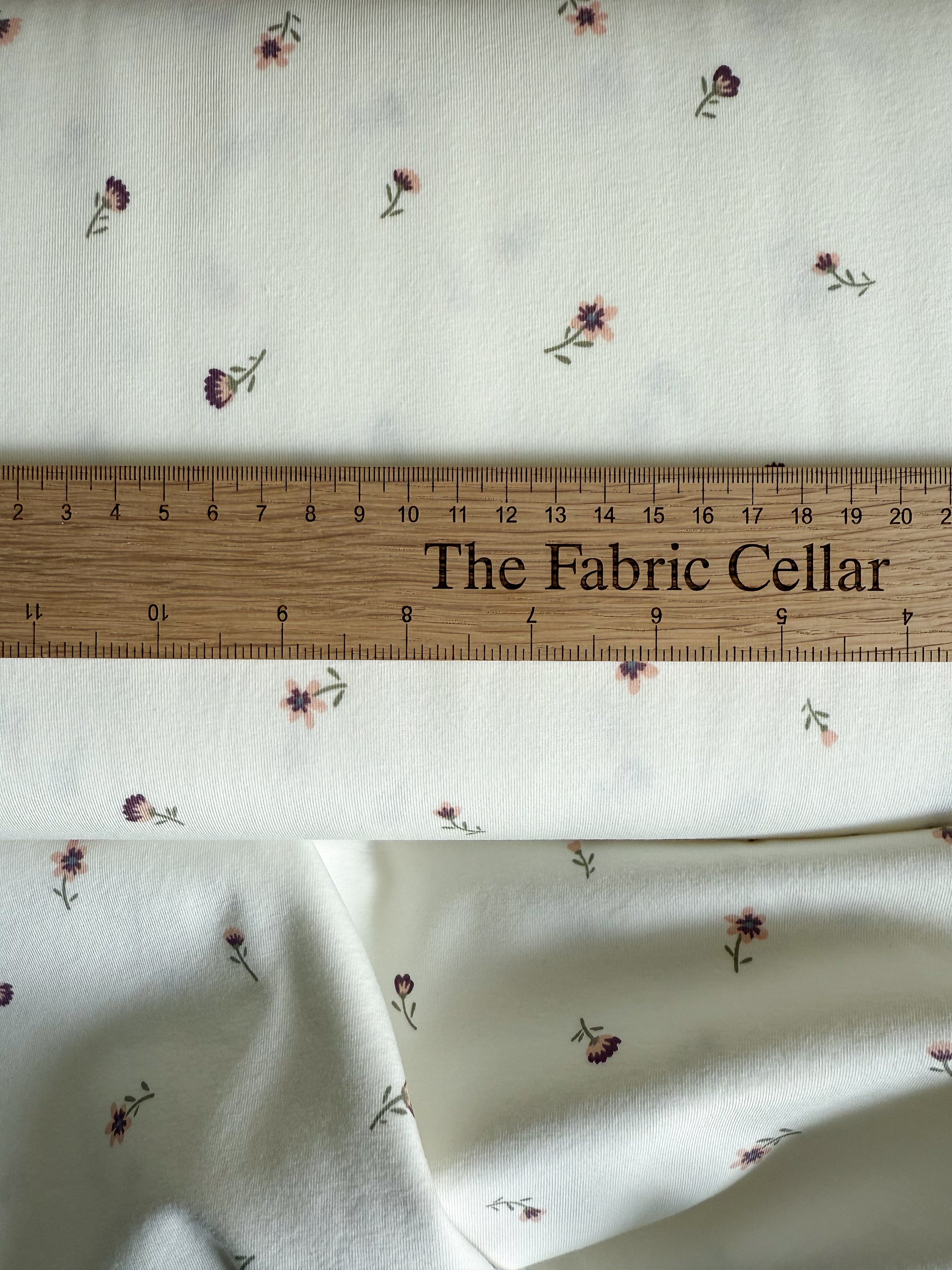 A pretty off-white cotton jersey fabric with ditsy purple and pink flowers