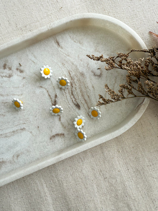 A small shank button in the shape of a yellow and white daisy. 
