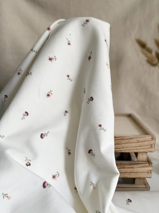 A pretty off-white cotton jersey fabric with ditsy purple and pink flowers