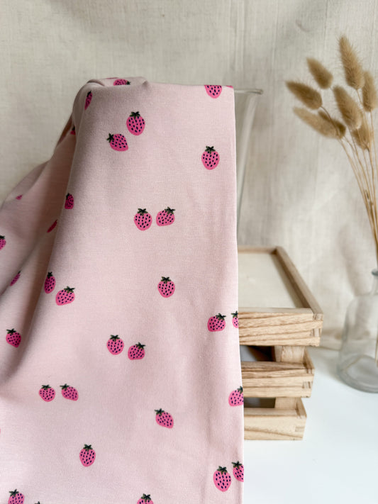 Pink fabric with black and red berry pattern draped over a surface with a neutral background.