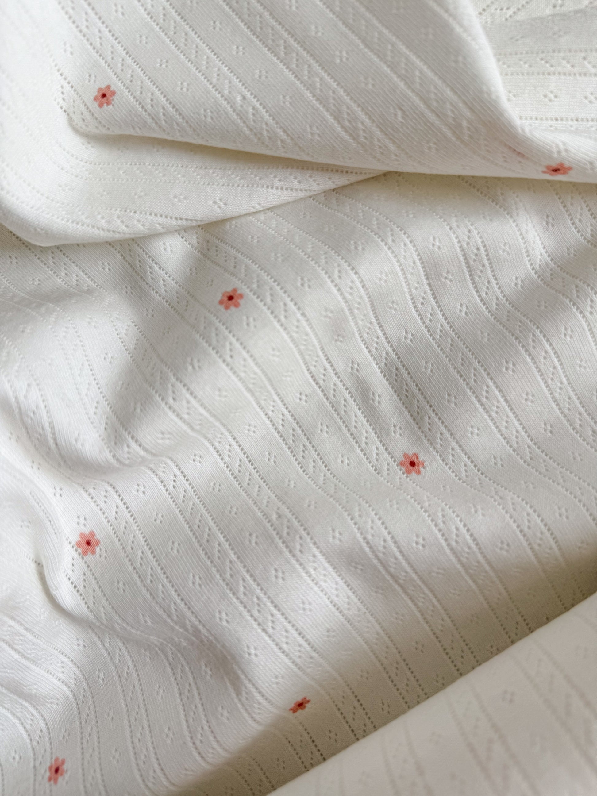 Tiny pink flowers on a white pointelle jersey fabric for sewing T-Shirts and Baby Clothing and Pyjamas