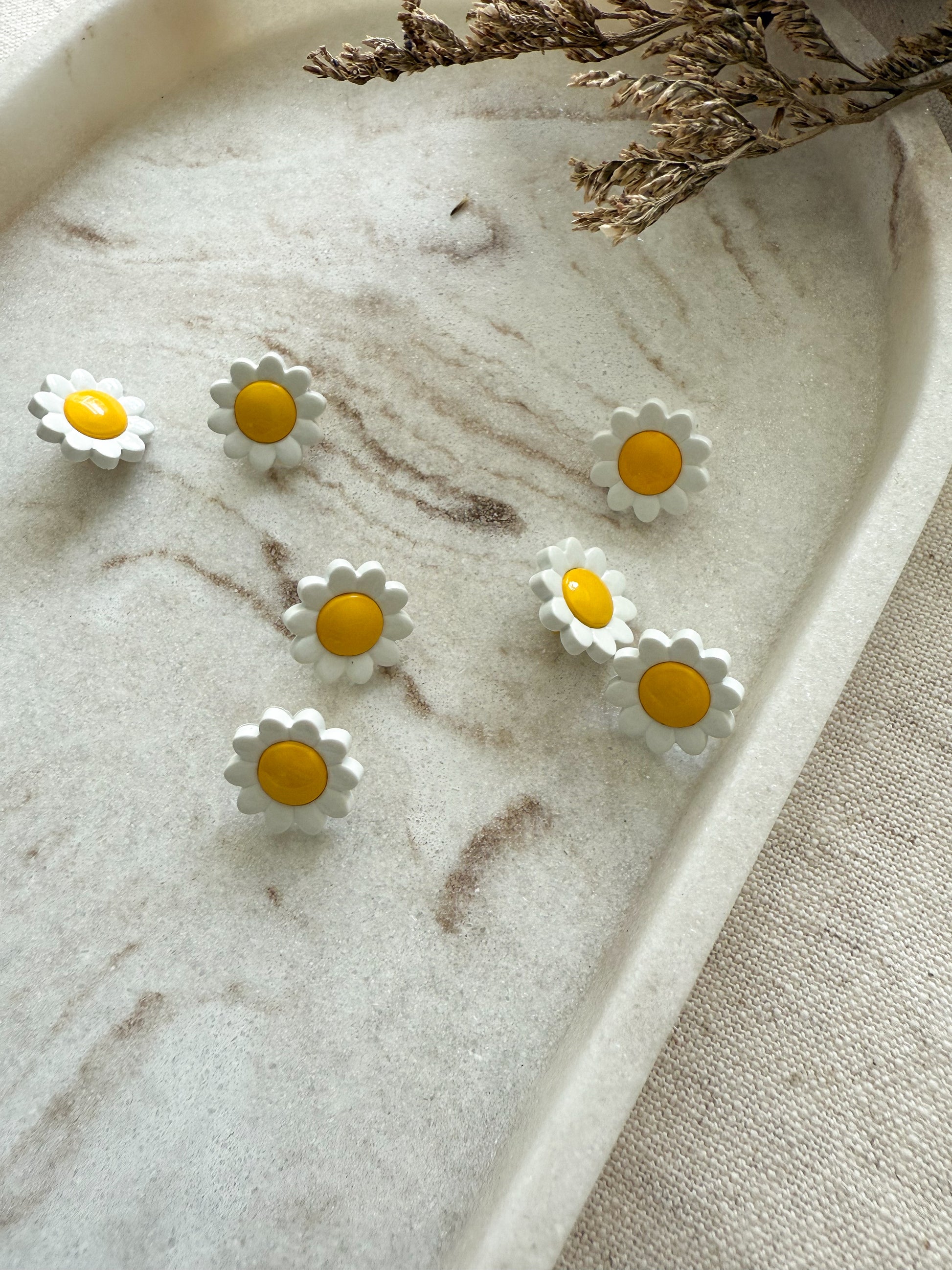 A small shank button in the shape of a yellow and white daisy. 