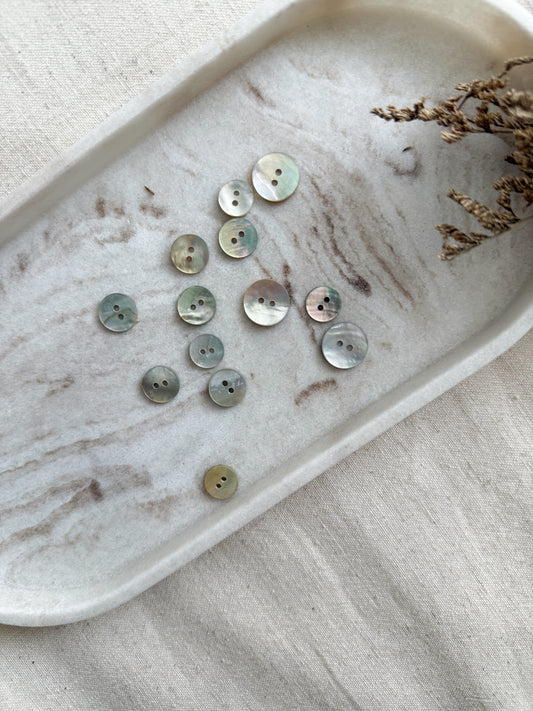 A natural mother of pearl sewing button with two holes in a number of sizes